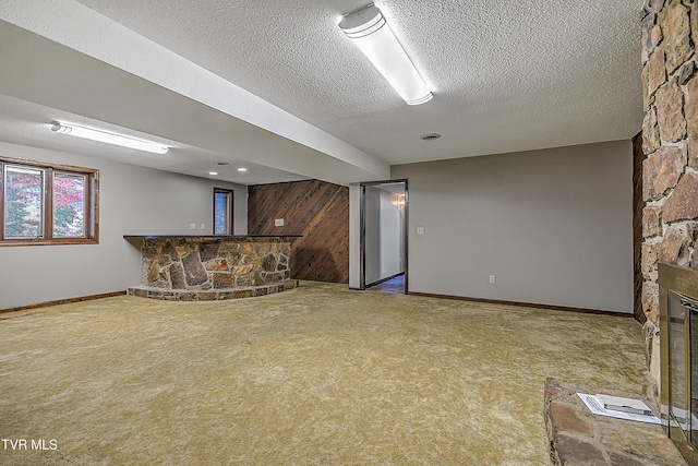 unfurnished living room featuring carpet flooring, a textured ceiling, a stone fireplace, and wooden walls