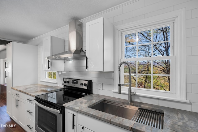 kitchen with stainless steel range with electric stovetop, wall chimney exhaust hood, white cabinets, and plenty of natural light