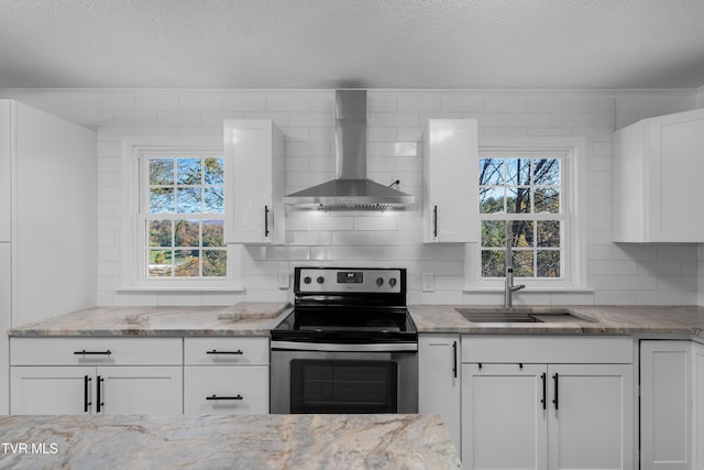 kitchen with wall chimney exhaust hood, a wealth of natural light, white cabinets, and stainless steel electric range oven