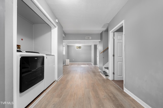 corridor with a textured ceiling, light hardwood / wood-style flooring, and separate washer and dryer