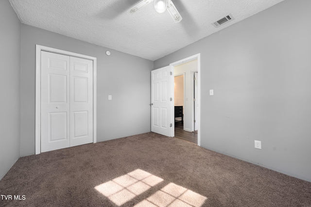 unfurnished bedroom with a closet, ceiling fan, a textured ceiling, and dark carpet