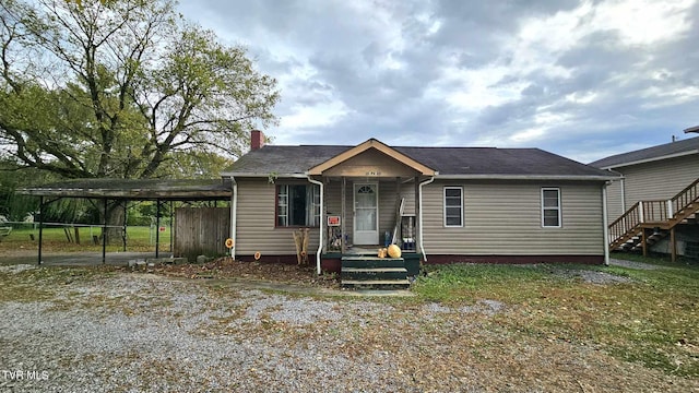 bungalow-style home with a detached carport, gravel driveway, a chimney, and fence