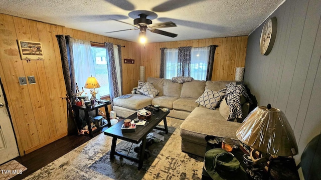 living room featuring dark wood-type flooring, wood walls, ceiling fan, and a textured ceiling