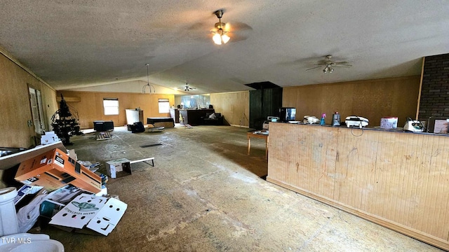 interior space featuring ceiling fan, a textured ceiling, wooden walls, and vaulted ceiling