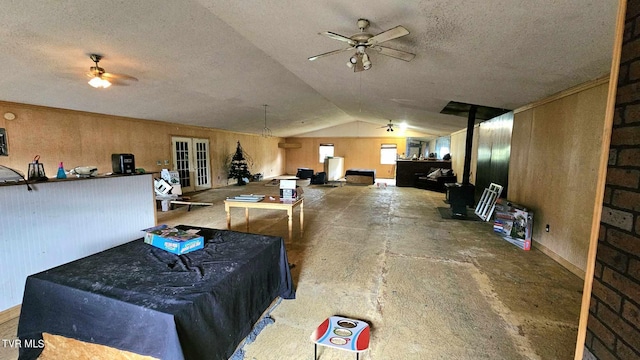 misc room featuring wood walls, concrete flooring, lofted ceiling, french doors, and a textured ceiling