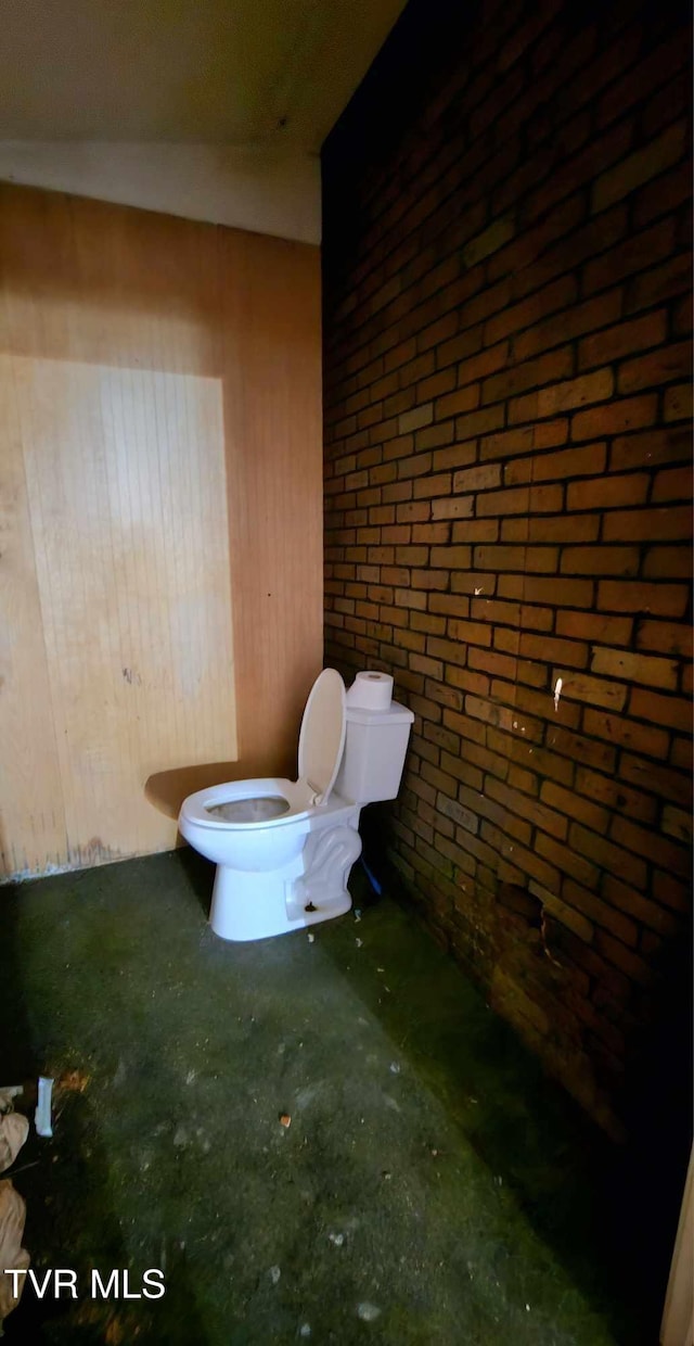 bathroom featuring wood walls, toilet, brick wall, and concrete floors