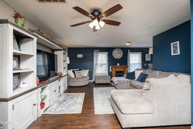 living room featuring ceiling fan, a textured ceiling, and dark wood-type flooring