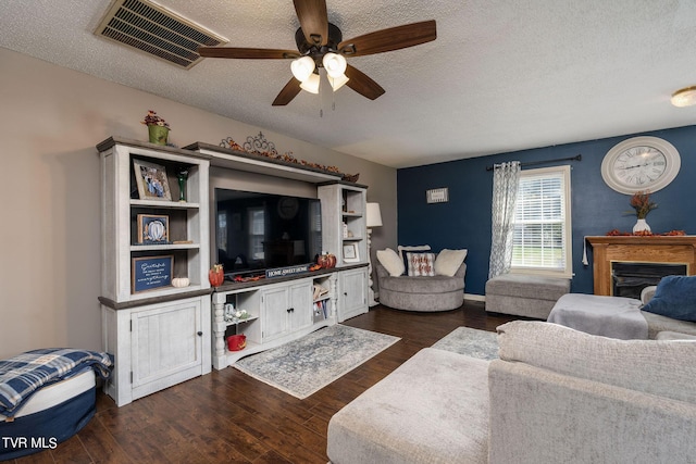 living area with ceiling fan, a fireplace, a textured ceiling, visible vents, and dark wood-style floors