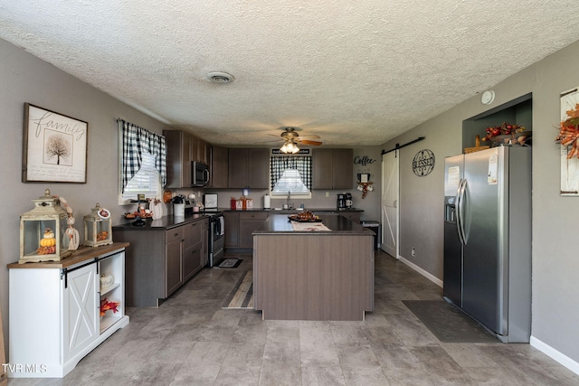 kitchen featuring ceiling fan, a textured ceiling, stainless steel appliances, a center island, and a barn door