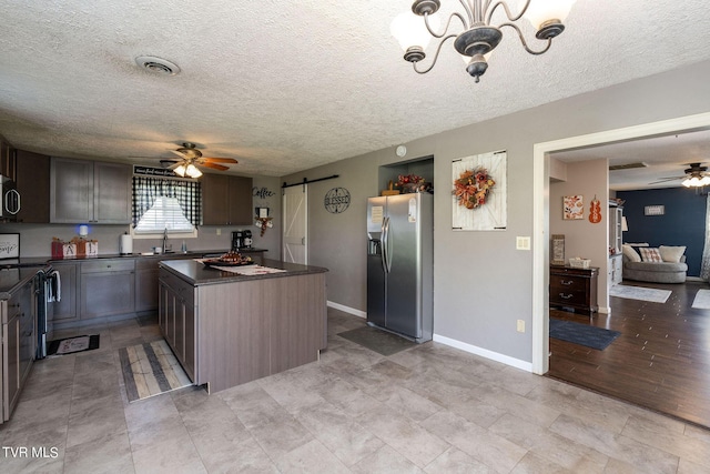 kitchen with ceiling fan with notable chandelier, stove, a barn door, stainless steel refrigerator with ice dispenser, and dark countertops