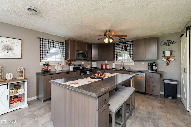 kitchen with a kitchen island, ceiling fan, stainless steel appliances, sink, and a kitchen breakfast bar