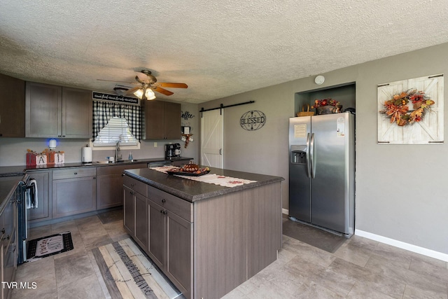 kitchen with ceiling fan, a barn door, a center island, dark countertops, and stainless steel fridge