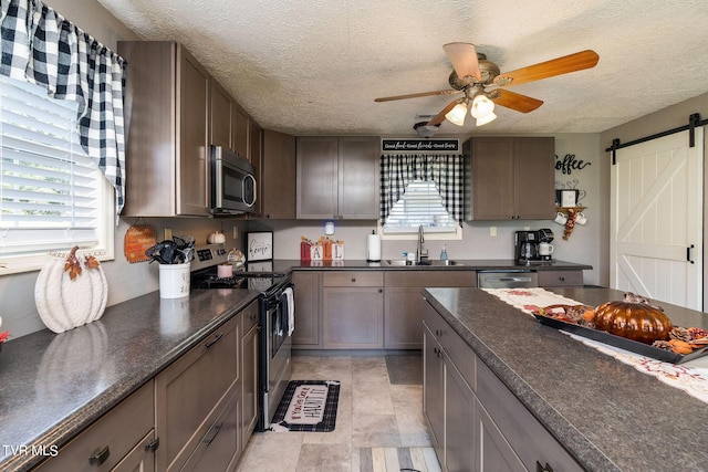 kitchen featuring a textured ceiling, a barn door, appliances with stainless steel finishes, dark countertops, and a sink