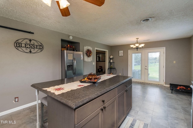 kitchen with a textured ceiling, stainless steel refrigerator with ice dispenser, a center island, dark countertops, and french doors