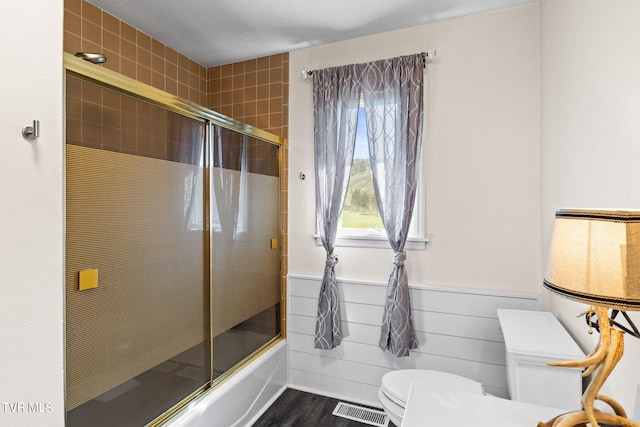 bathroom with shower / bath combination with glass door, hardwood / wood-style floors, and toilet