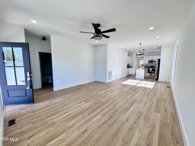 unfurnished living room featuring ceiling fan with notable chandelier and light wood-type flooring