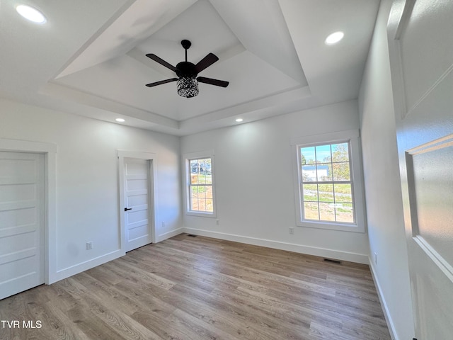 unfurnished bedroom with ceiling fan, a raised ceiling, and light wood-type flooring