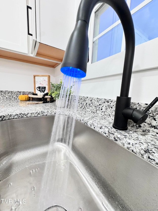 room details with white cabinetry, sink, and light stone counters