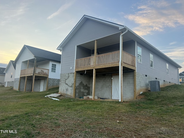 back house at dusk with central AC, a lawn, and a balcony