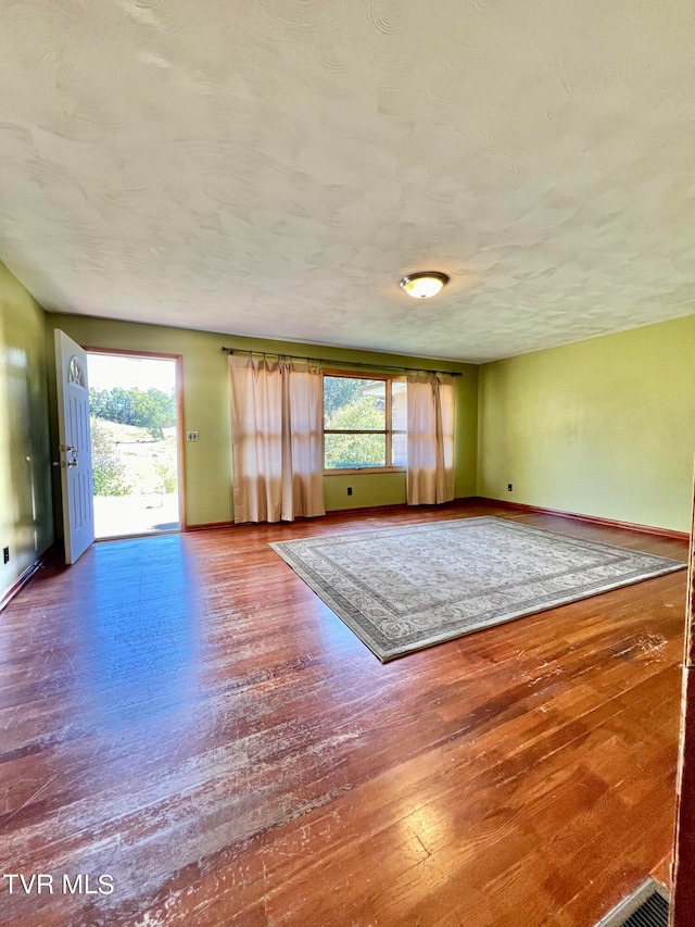 empty room with a textured ceiling, hardwood / wood-style flooring, and plenty of natural light