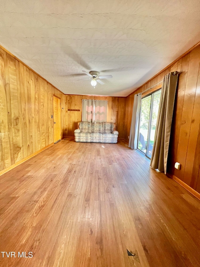 unfurnished living room with ceiling fan, wood walls, and hardwood / wood-style floors