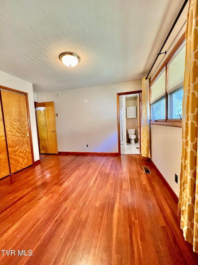 unfurnished bedroom featuring hardwood / wood-style floors, a textured ceiling, and ensuite bath