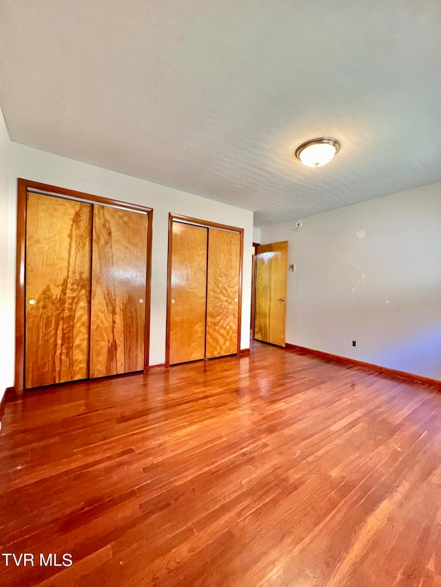 unfurnished bedroom with hardwood / wood-style floors, two closets, and a textured ceiling