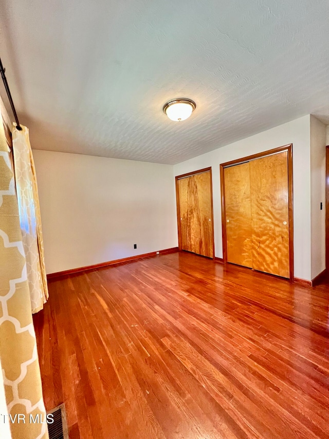 unfurnished bedroom featuring a textured ceiling, two closets, and hardwood / wood-style flooring