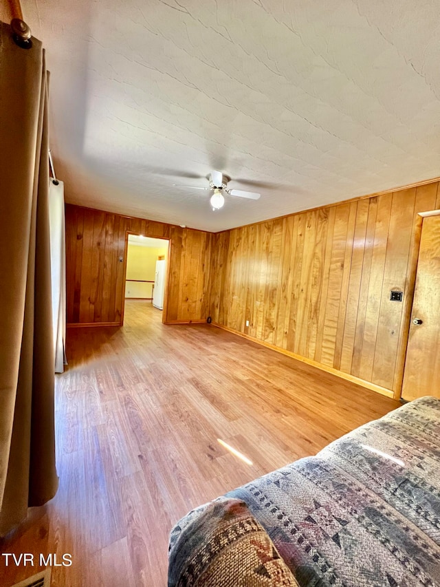 interior space with ceiling fan, hardwood / wood-style flooring, and wood walls