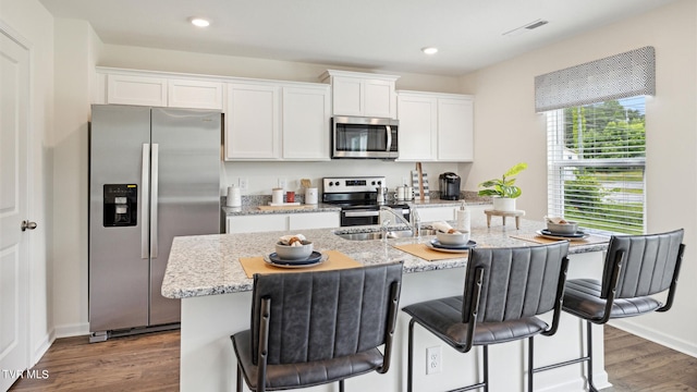 kitchen with light stone counters, white cabinetry, appliances with stainless steel finishes, and an island with sink