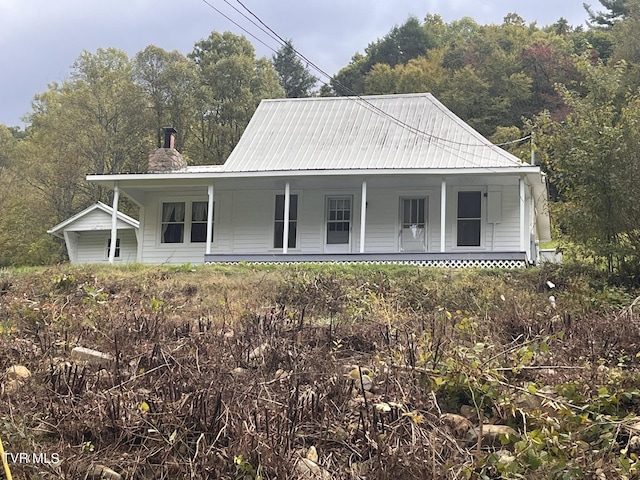 view of front of home featuring covered porch, a chimney, and metal roof