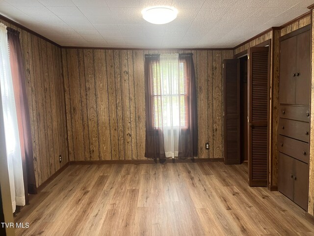 unfurnished bedroom with wooden walls, baseboards, and light wood-style flooring