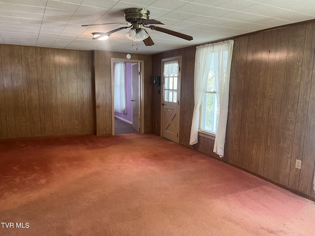 empty room with baseboards, carpet flooring, ceiling fan, and wood walls