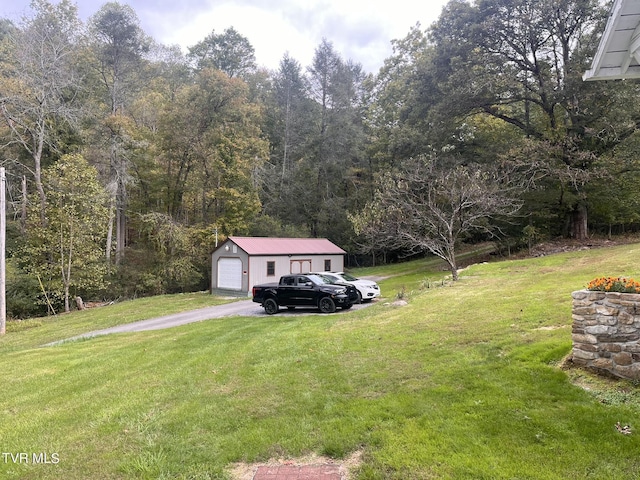 view of yard with a garage, an outdoor structure, driveway, and a forest view