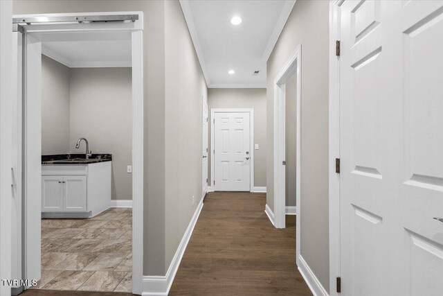 hallway with light wood finished floors, baseboards, ornamental molding, a sink, and recessed lighting