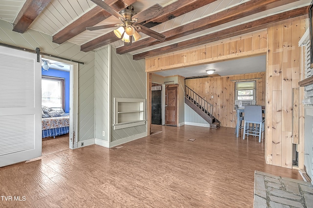 unfurnished living room with wood-type flooring, a wealth of natural light, wooden walls, and a barn door