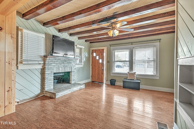 unfurnished living room featuring wood ceiling, beamed ceiling, a brick fireplace, light hardwood / wood-style floors, and wood walls