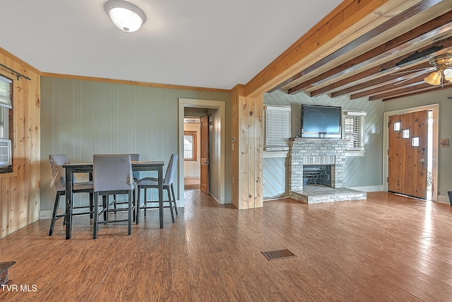 interior space with hardwood / wood-style flooring, beam ceiling, wooden walls, a wealth of natural light, and a fireplace