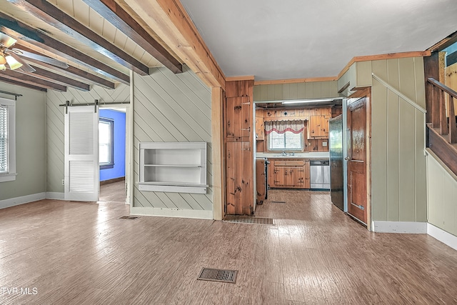 kitchen featuring beamed ceiling, wooden walls, wood-type flooring, a barn door, and stainless steel dishwasher