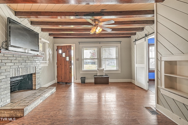 unfurnished living room with beamed ceiling, a barn door, hardwood / wood-style flooring, and wooden walls