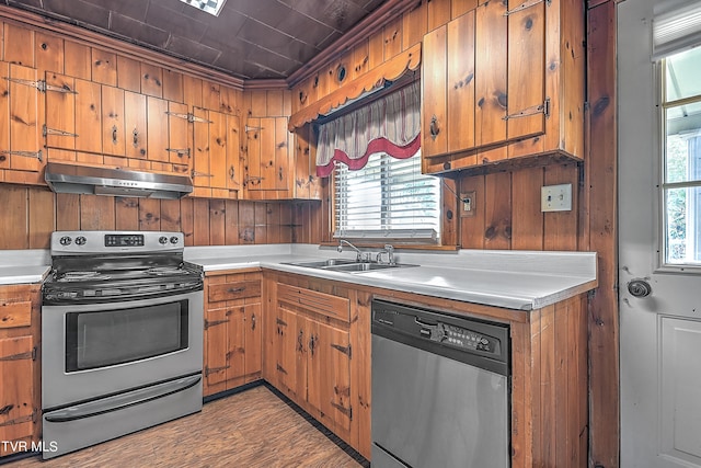 kitchen with sink, appliances with stainless steel finishes, light hardwood / wood-style floors, and wood walls