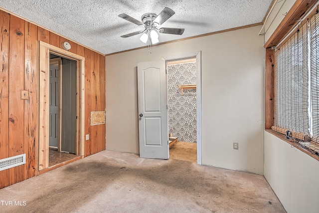 unfurnished bedroom featuring ceiling fan, wood walls, a textured ceiling, and light colored carpet