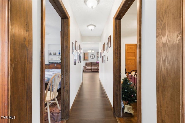 corridor with dark hardwood / wood-style floors and a chandelier