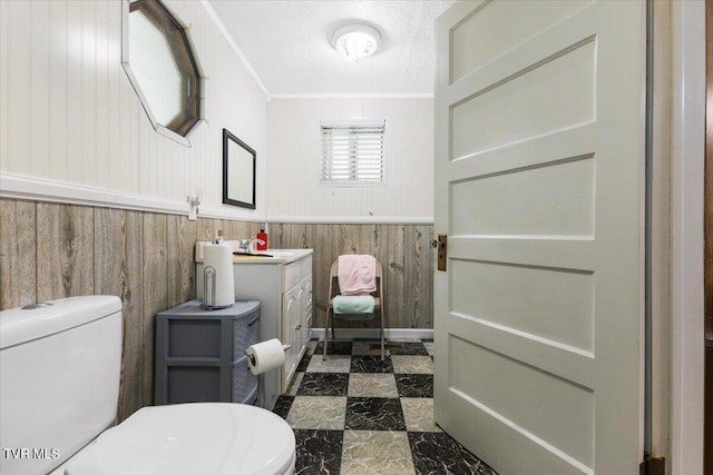 bathroom with a textured ceiling, toilet, wood walls, ornamental molding, and vanity