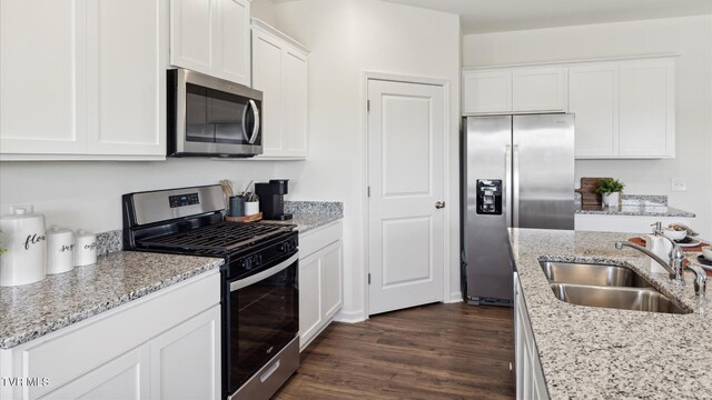 kitchen with dark wood-style flooring, stainless steel appliances, white cabinetry, a sink, and light stone countertops