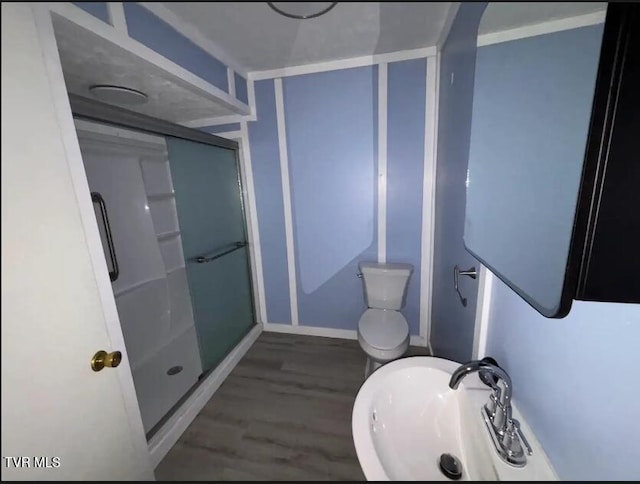 bathroom with sink, a shower with shower door, hardwood / wood-style flooring, and toilet