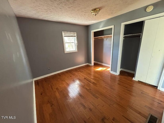 unfurnished bedroom featuring a textured ceiling, two closets, and wood-type flooring