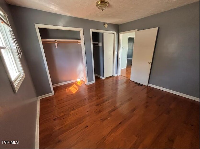 unfurnished bedroom featuring a textured ceiling, two closets, and hardwood / wood-style flooring