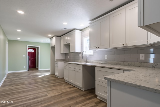 kitchen featuring dark wood-type flooring, sink, white cabinetry, light stone counters, and a textured ceiling