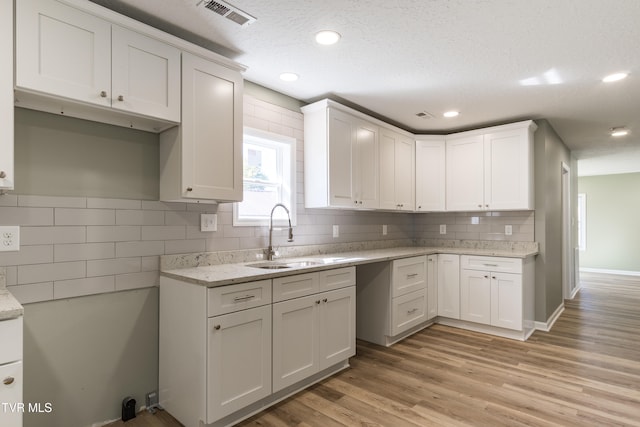 kitchen with white cabinets, tasteful backsplash, a textured ceiling, light wood-type flooring, and sink